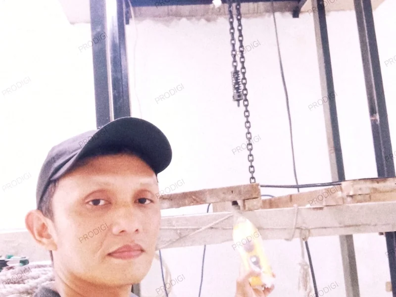 Teknisi Prodigi memegang pendant controller lift barang dengan electric chain hoist di atas